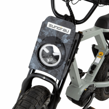 Close-up of the front headlight of the EUNORAU e-bike, featuring a rugged camo-patterned headlight cover, highlighting the bikeâ€™s durable and stylish design.