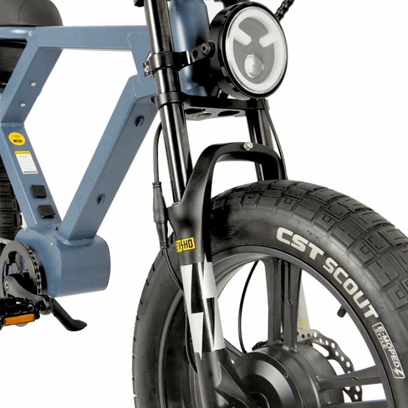 Close-up of an e-bike's front end, featuring a CST Scout tire, suspension fork, and integrated headlight, designed for stability and visibility on various terrains.