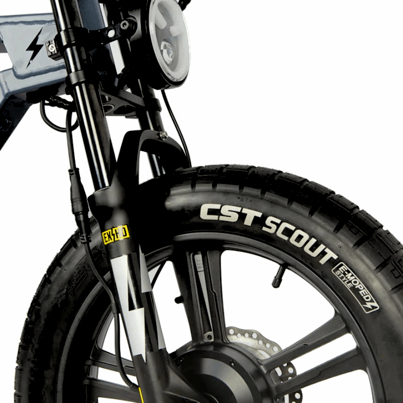 Close-up of an e-bike's front suspension, CST Scout tire, and integrated headlight, highlighting the robust design and enhanced visibility for various terrains.